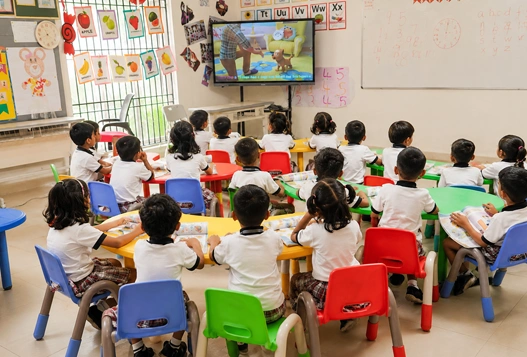Early years 2 kids engaged in play-based learning activities while watching a video on TV.